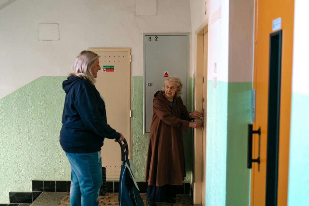 An elderly woman and her caregiver interact in a building hallway in Prague, Czech Republic.